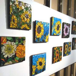 Ten colorful mosaic tiles featuring various flower designs are displayed on a white wall in two rows.
