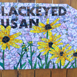 Mosaic art sign with the words “BLACK EYED SUSAN” and yellow black-eyed Susan flowers on a purple background.