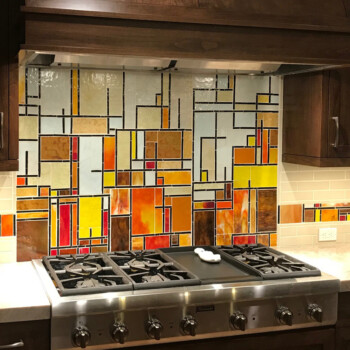 SOLD A kitchen stove with a colorful, geometric stained glass backsplash and dark wooden cabinets.