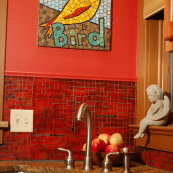 SOLD A kitchen sink with red mosaic backsplash, apples on the counter, and a mosaic bird artwork labeled "Bird" on the wall.