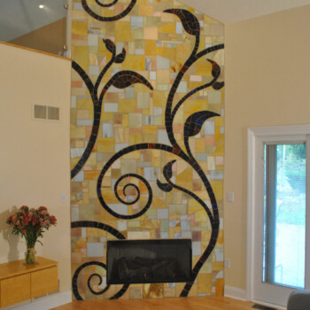 SOLD Fireplace wall with yellow mosaic tiles and large black swirling vine design, in a modern living room with wood flooring.