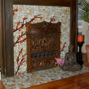 SOLD Decorative fireplace with mosaic tile, ornate metal screen, Buddha statue, pink flowers, candles, and potted plant.