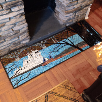 SOLD Rectangular mosaic depicting a white ship on blue water with trees in the foreground, placed in front of a stone fireplace.