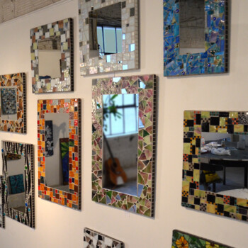 A wall displays several rectangular mirrors, each framed with colorful mosaic tiles in various patterns and colors.