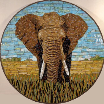 SOLD Round mosaic artwork of an elephant with large ears, tusks, and grass in the foreground against a blue sky background.