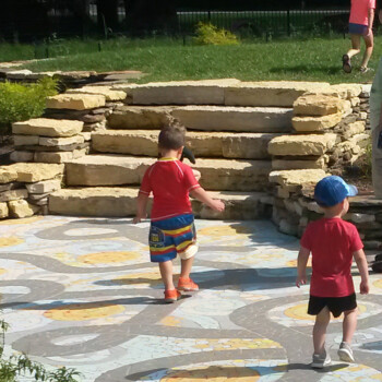 SOLD Two young boys walk on a mosaic path near stone steps outside, accompanied by an adult and another child.