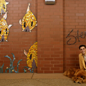 SOLD A man kneels beside a dog near a brick wall with fish mosaics and graffiti that says "Stevo.