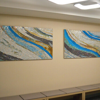SOLD Two abstract mosaic artworks with blue, white, and gold curves hang on a beige wall above a bench.
