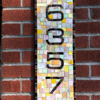 A mosaic tile sign displaying the number 6307 is mounted on a red brick wall.