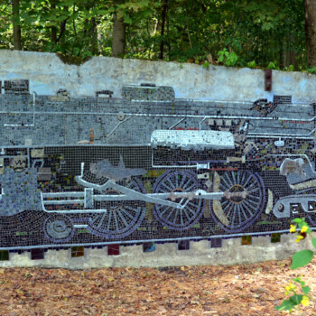 A mosaic mural of a steam locomotive engine displayed on an outdoor wall surrounded by trees and plants.