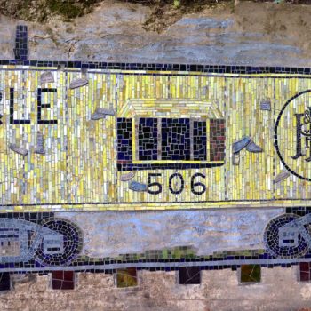 Mosaic mural of a yellow P&LE train boxcar with number 506 and scattered white feathers on a concrete wall.