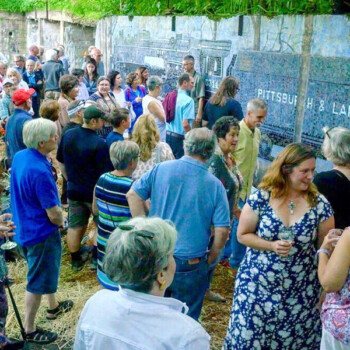 A group of people gather outdoors near a mural that reads "Pittsburgh & Lake Erie" on a sunny day.